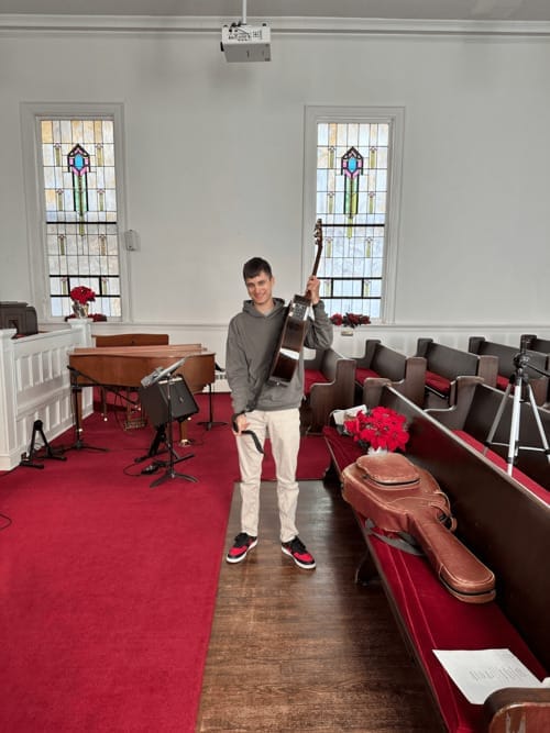 A young musician standing with a guitar in the First Baptist Church sanctuary